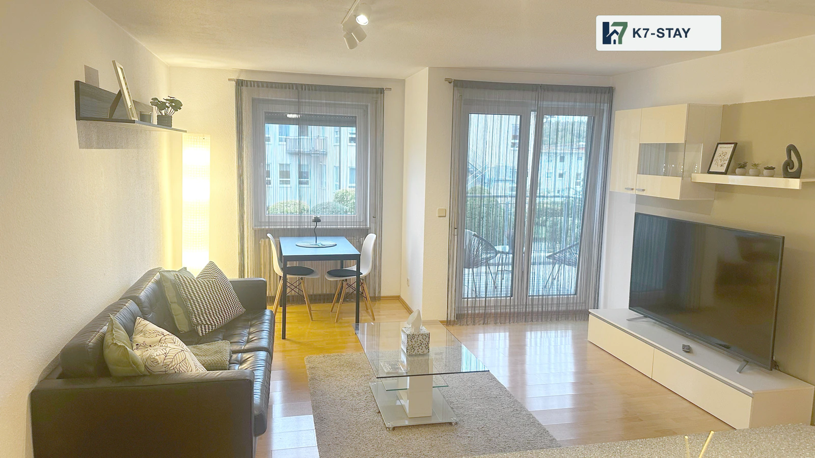 Wohnbereich mit Sofa, Fernseher und Zugang zum Balkon